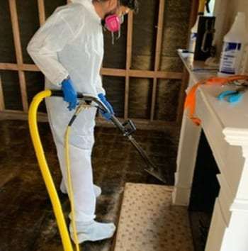 Technician in a protective suit cleaning a soot-stained wall