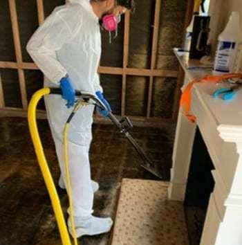 Technician in a protective suit cleaning a soot-stained wall