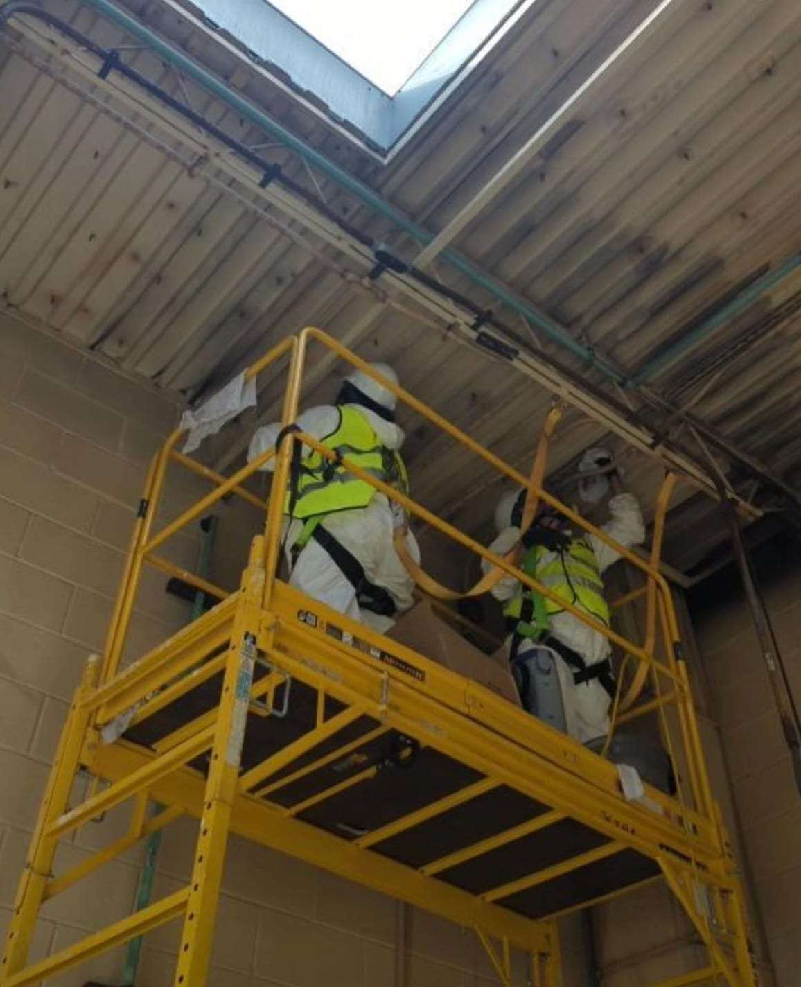 Technicians in protective suits on scaffolding cleaning a high ceiling